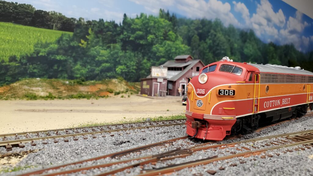Model train on tracks near rural backdrop.